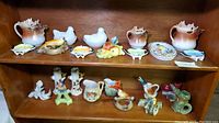 Wide view showing the full collection of vintage ceramics arranged on shelves, including moose pitchers, hen on nest dishes, teabag holders, and bird figurines.