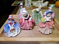 All six Royal Doulton Southern Belle figurines displayed on wooden tray showing variety of poses and colorful dresses.