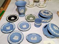 Overview of nine jasperware pieces including plates, urn, tumbler, lidded box in blue, green, and black with white relief classical designs.