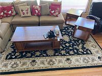 Living room setup showing the Kaleen Bombay rug under wooden coffee and side tables with sofa and cushions nearby, illustrating the rug's color and size context.