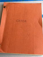Front cover of the bound script showing orange cover with "GATOR" stamped on the front secured with brass fasteners.