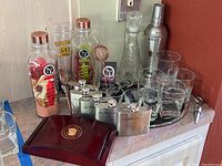 Wide angle photo showing full barware collection on a mirrored tray, including the martini shaker, decanter, shot glasses, flasks, and wine opener box.