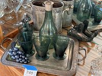 Lot shows green tinted glass carafe and six matching glasses displayed on the larger silver plated tray with embossed grape decor. Metal wine bottle holders and carved stone fish sculpture accompany setup.