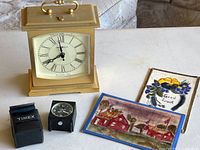 Photo showing Howard Miller Westminster carriage clock, miniature Timex clock with leather case, and two antique fabric postcards