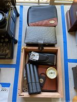 Photo showing two storage cases and assorted smoking-related items, including a hygrometer and a metal flask.