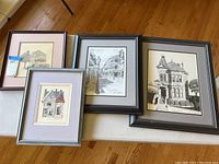 Four framed art prints displayed on a table including three Victorian homes and one New Orleans home.