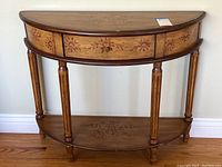 Full view of the half round wooden side table with decorative floral carvings on drawer, shelf and top.