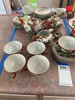 First photo showing two porcelain tea pots, sugar bowl, creamer, five tea cups, and six small plates with Japanese theme decoration