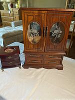 Two wooden jewelry boxes on a white cloth background showing overall size difference and detailed front design of floral glass doors and drawers.