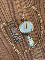 Full lot showing pocket watch with attached chain, cloisonné money clip, and Mickey Mouse cloisonné pin on wooden surface.