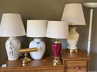Photo of six lamps arranged on dresser top including four table lamps, one brass desk lamp, and one torchiere floor lamp