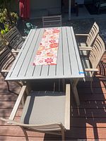 Photo of the rectangular metal patio table with six chairs on a wooden deck, shows table surface and design of chair seats and backs, illustrating weathering and fading.
