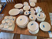 Full overview of the china set laid out on wooden table with plates, cups, serving bowls, coffee pot, and storage cases
