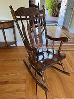 Full view of the wooden rocking chair showing the seat, armrests, and rocker legs on wood floor.