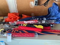 Photo showing 16 umbrellas in various colors stacked together, some with visible sports logos or color patterns.