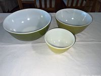 Three nested Pyrex mixing bowls with green exterior and white interior, largest bowl is around 10 inches diameter.