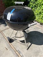 Full view of black Weber charcoal kettle grill showing lid, handle, stands, and wheels outdoors.