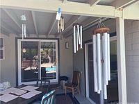 Outdoor patio area with multiple wind chimes hanging from ceiling beams, view includes sliding door and chairs