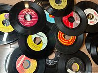 Close-up image showing multiple 45 RPM vinyl records with various labels, including Apex, Monument, and Columbia, placed overlapping on a surface.