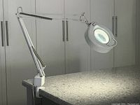 Adjustable desk lamp with magnifying lens and ring light mounted on a countertop with clamp base, arm extended horizontally.