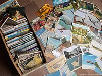 Box filled with tightly packed postcards, some spilling out depicting various landscapes, vehicles, and animals.