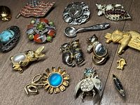 Overhead image showing entire assortment of 15 mixed vintage brooches of various designs and colors on wooden surface.