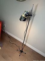 Full view of the mid-century adjustable floor lamp standing upright, showing the vertical pole, adjustable head and four-legged base on wood floor near wall.