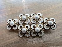 Front view of enamel and silver brooch showing five connected flower shapes with white enamel petals and silver centers.