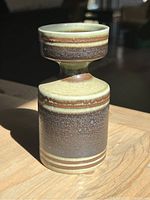 Side view of vase with layered earthy glazes and banded pattern in natural light.