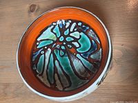 Top view showing bright orange interior and multicolored abstract floral pattern on bowl base.