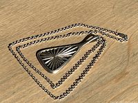 Full view of the silver pendant laying on the silver chain, clearly showing the modern geometric pattern on the front side of the pendant.