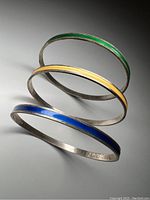 Three vintage David-Andersen sterling silver bangles with colored enamel bands in green, yellow, and blue, stacked in a group on a white surface.