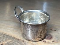 Side view showing the cup's shape, handle with ornate detail, and surface wear.