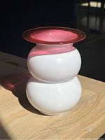 Side view of the white glass vase with double rounded bulb shape and pink flared rim on a wooden surface.