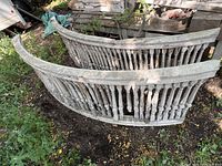 Two curved wooden Victorian banister railings outdoors on grass with multiple turned spindles and chipped white paint.