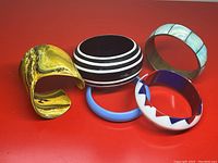 Five vintage bracelets displayed on red surface, showing different colors and patterns: striped, marbled, solid blue, geometric red/white/blue, and marbled blue/white.
