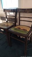 Pair of black wooden chairs with gold trim, each seat has a hand-painted jockey on horseback with the word "Hampton". The backrest reads "Winner Brighton 1851".