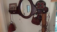 Full view of wooden coat hanger with mirror, metal bell hanging on left, floral holder with baskets on right, and four pegs below mirror.