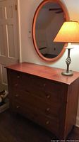 Wood Ethan Allen dresser with oval mirror and lamp, showing full height and furniture setup.