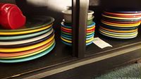 Stack of colorful Fiesta Ware plates and bowls on dark wooden shelving, showing size variations and vibrant colors.
