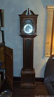 Full view of tall wooden grandmother clock showing upper clock and lower cabinet door open