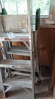 Photo showing folded aluminum ladder with visible wear and stains on steps and rails in garage setting