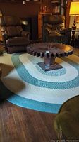 Full view of large oval woven area rug on wooden floor with coffee table and chairs on top showing size and color pattern.