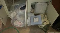 View of assorted bundled linens, towels, butterfly sheets, mattress protector under cabinet in basement.