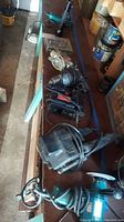 Multiple power tools lined up on a bench in a garage showing saws, drills and sanders with cords wrapped