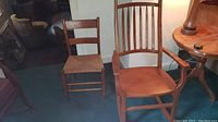 Photo showing both wooden chairs, one a rocking chair and the other a standard chair with woven seat, placed on a blue carpeted floor