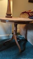 Full view of round wooden side table showing the tabletop and partial base with a lamp on top and couch nearby.