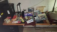 Desk surface with assorted office supplies including folders, calculators, pens, envelopes, tape dispensers, laser printer materials, and a desk lamp.