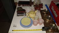 View of the tea set with teapot, cups, plates, and Elvis piano music box on table with measuring tape for scale