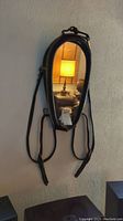 Horse bridle mirror hanging on the wall with visible leather straps, reflecting a lamp and room interior.